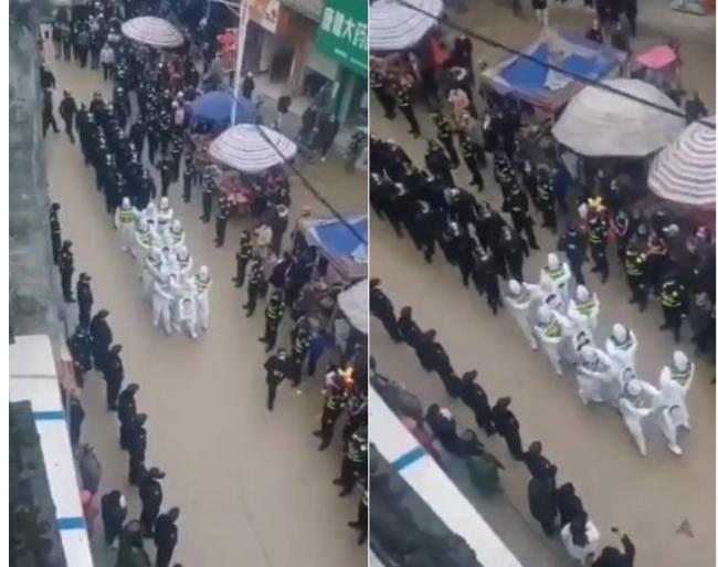 只见影中数名穿著白色隔离衣的人，双手被身边防疫人员抓住，身前还挂著一张大大的个人肖像，在公安人员监督下被逼得在大街上游街示众，旁边还一直不断播放呼吁遵守防疫措施的广播。（撷取自推特）